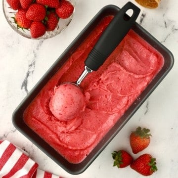 A scoop of strawberry sherbet on a container of ice cream.