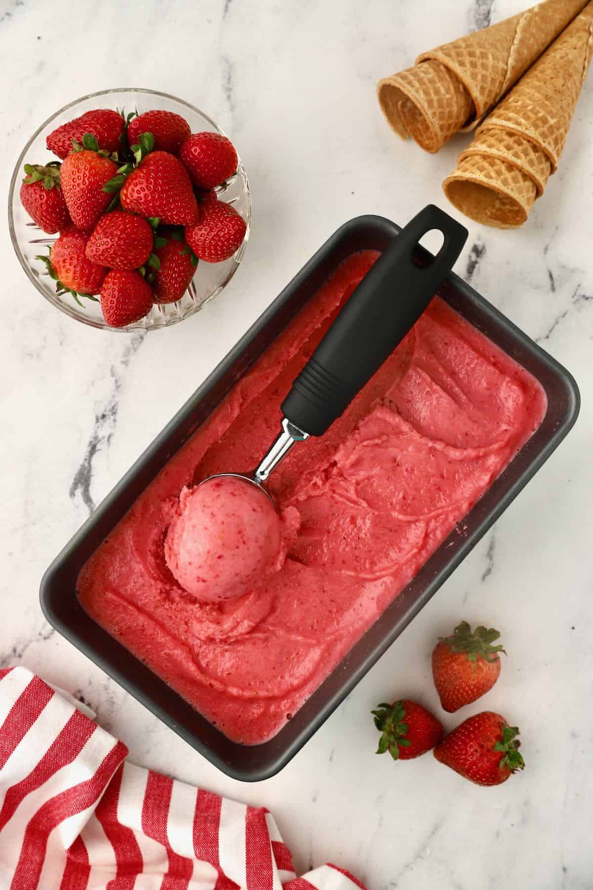 A scoop of strawberry sherbet  on a container of ice cream. 