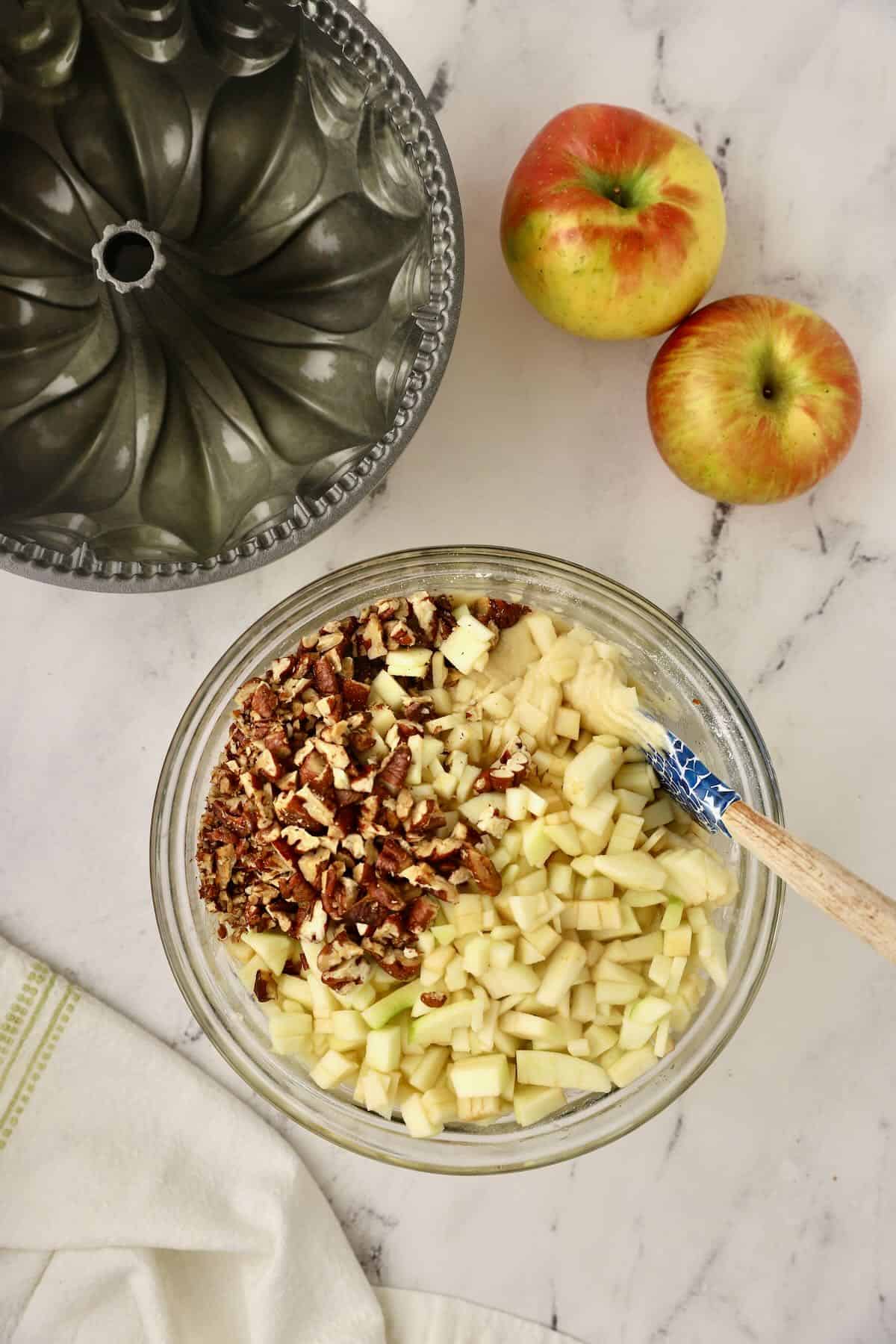 Chopped apples and pecans in a bowl with cake batter. 