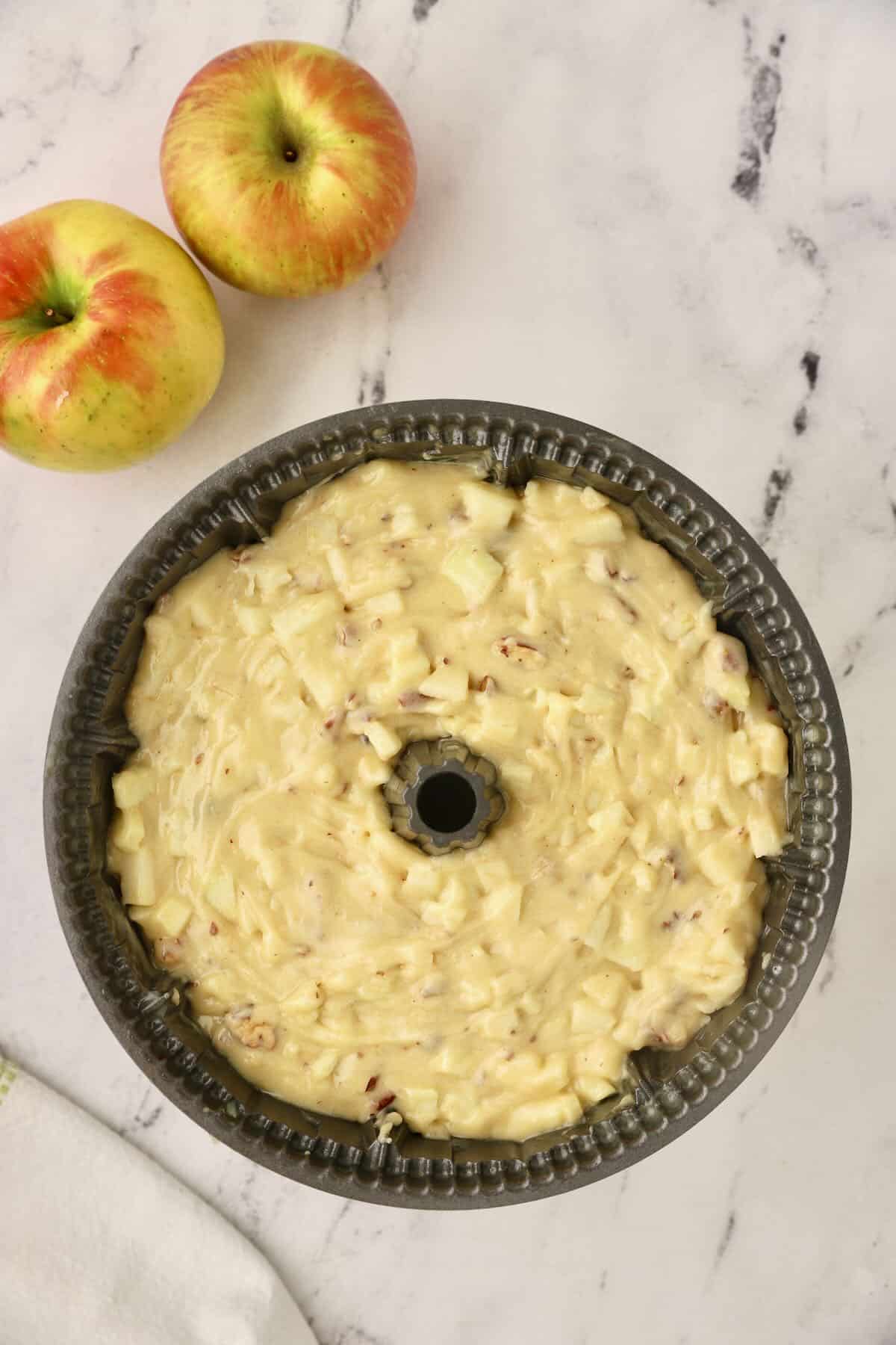 A bundt cake pan full of cake batter with cut up apples. 