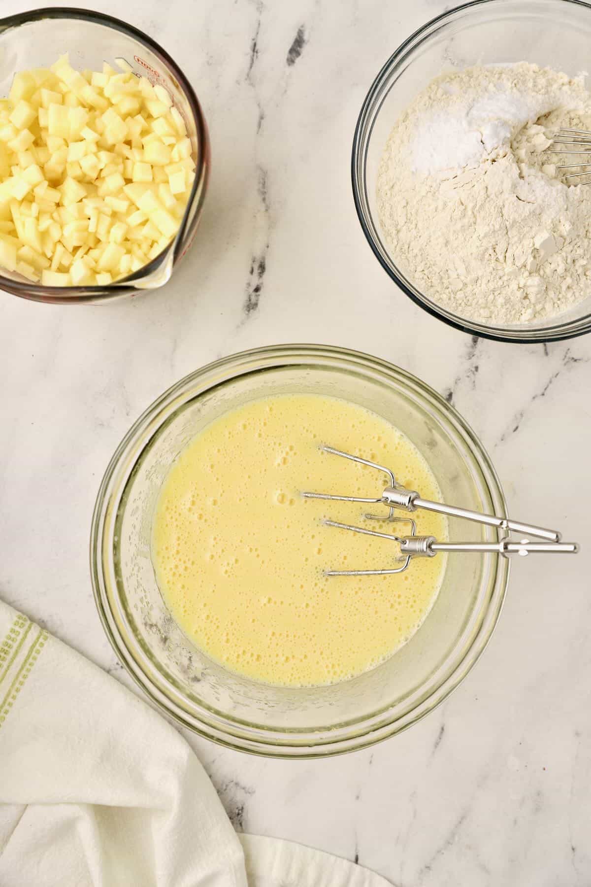 Electric mixer beaters in a bowl of oil, sugar, and eggs. 