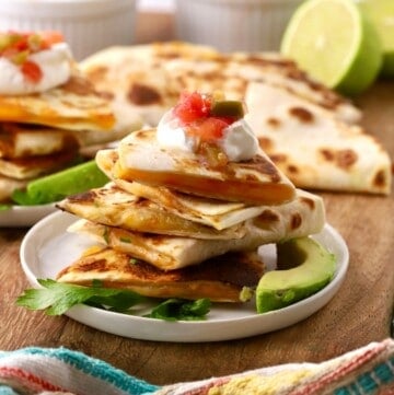 Four quesadillas in a stack topped with sour cream and salsa.