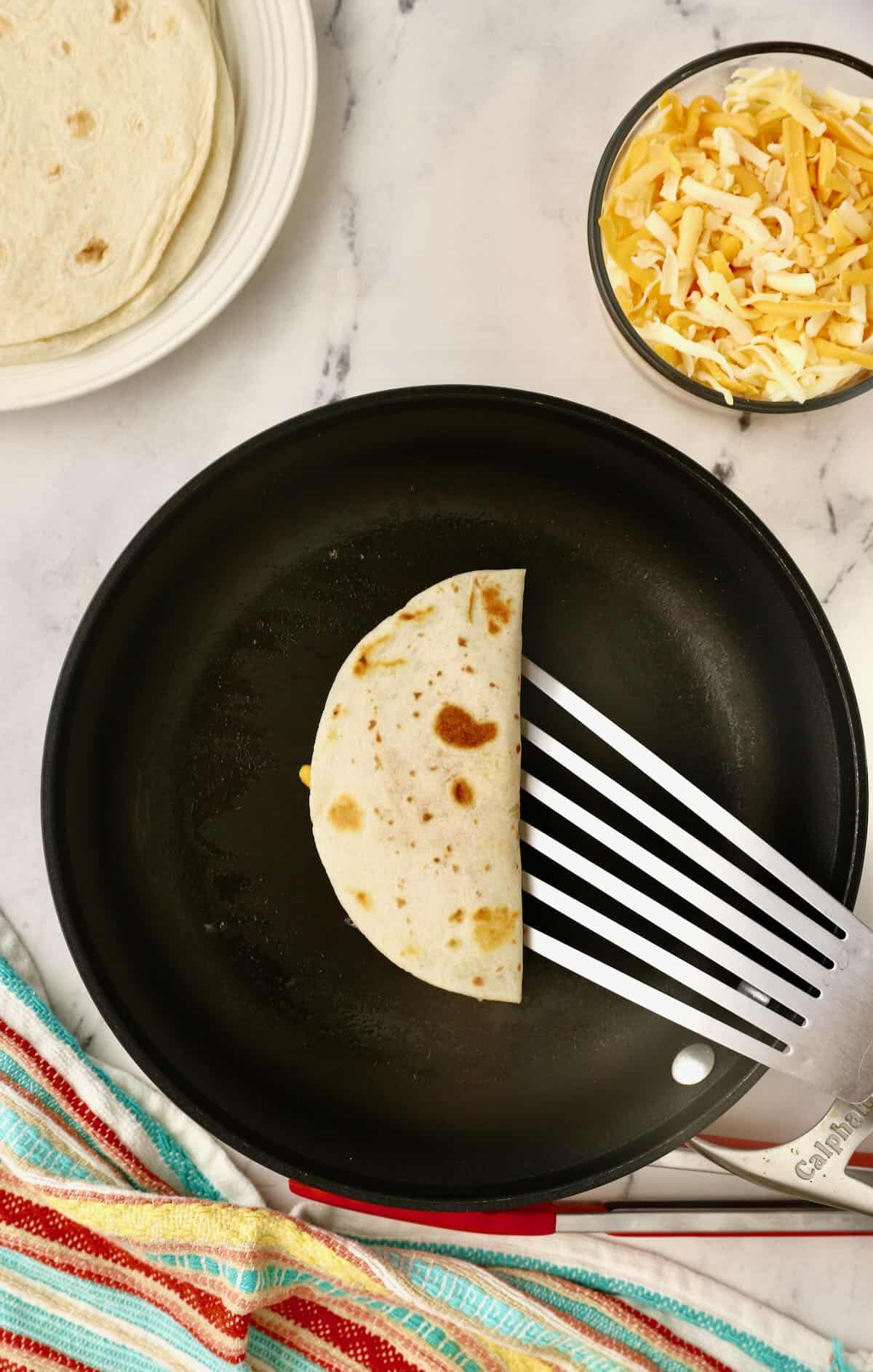 A cooked cheese quesadilla being removed from a skilled. 