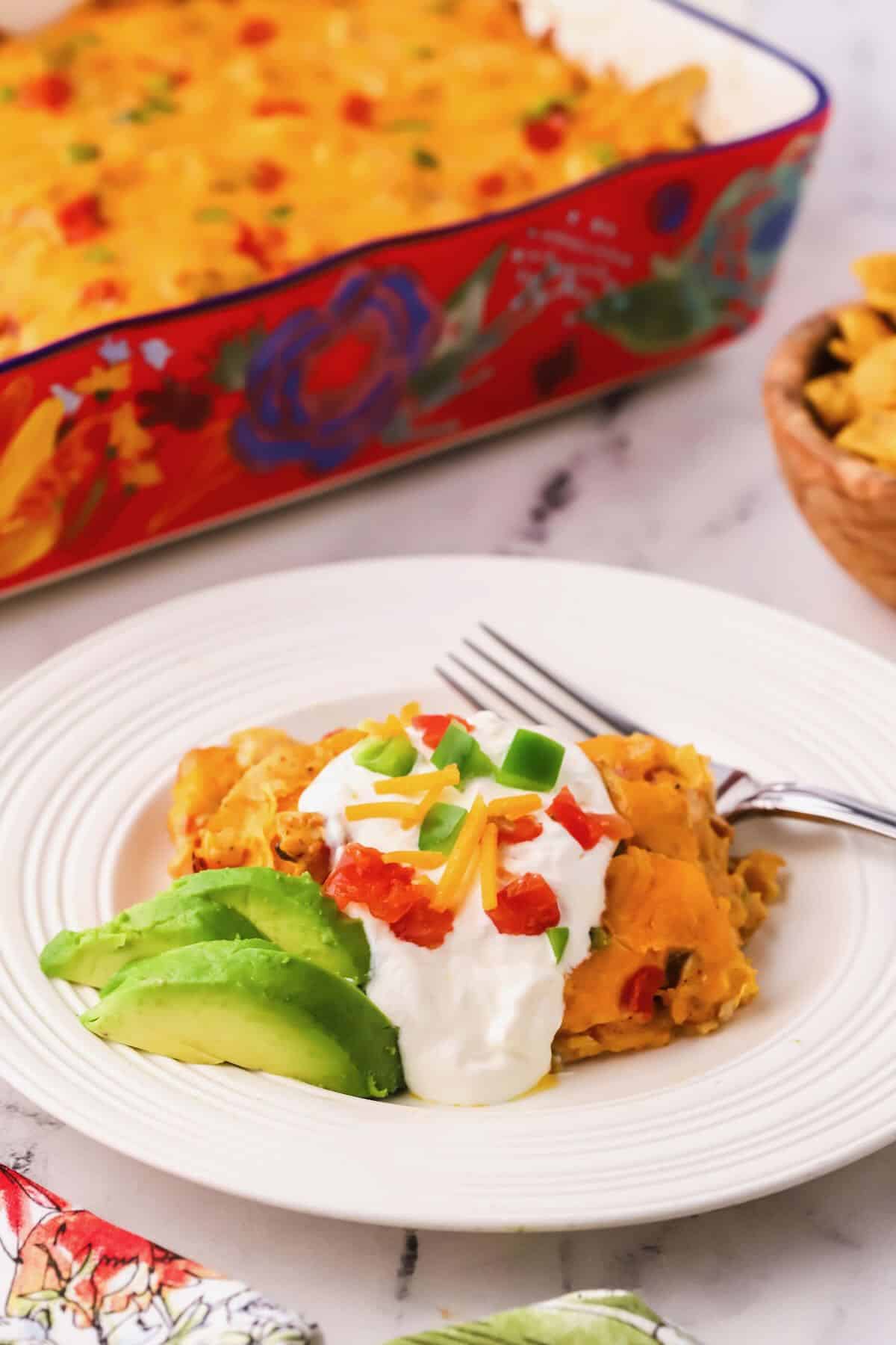 A serving of king ranch chicken casserole on a white plate topped with sour cream.  