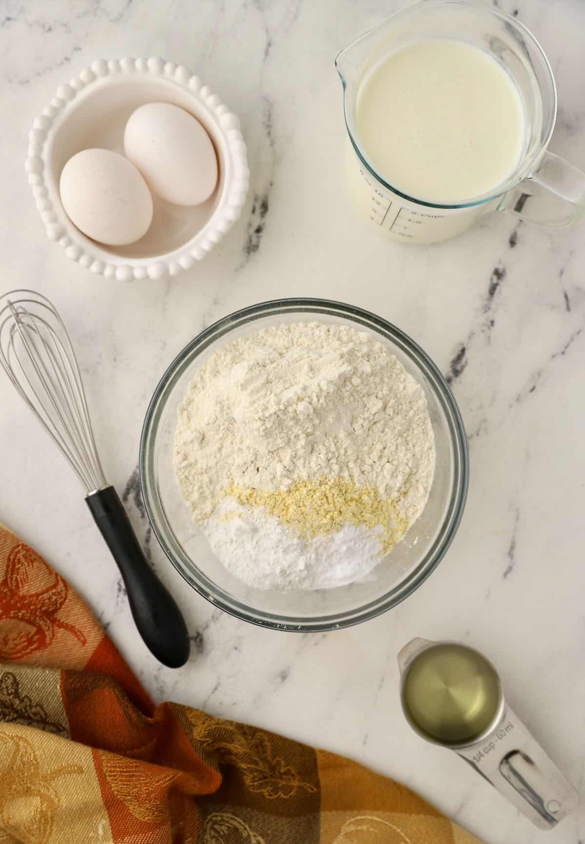 Cornmeal, flour, and baking powder in a clear glass bowl. 