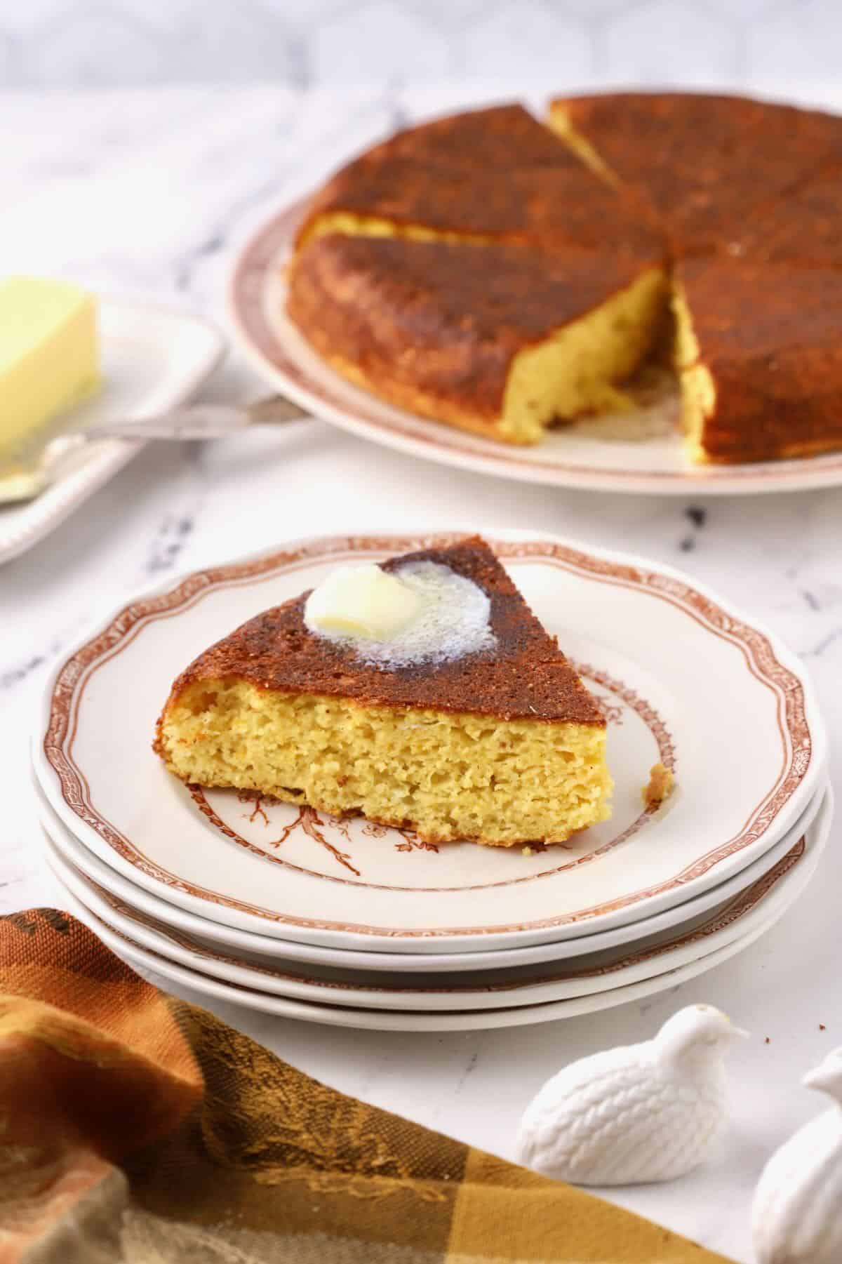 A slice of southern cornbread on a plate topped with butter. 