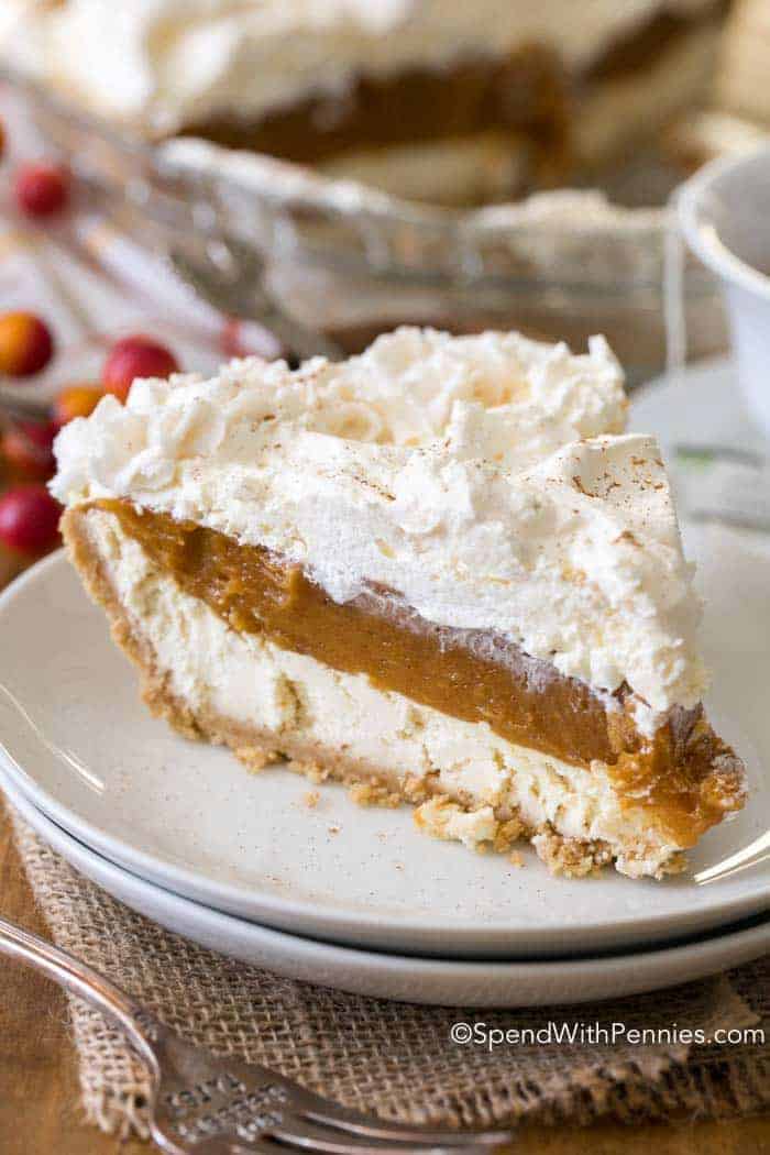 A slice of a layered pumpkin cheesecake topped with whipped topping. 