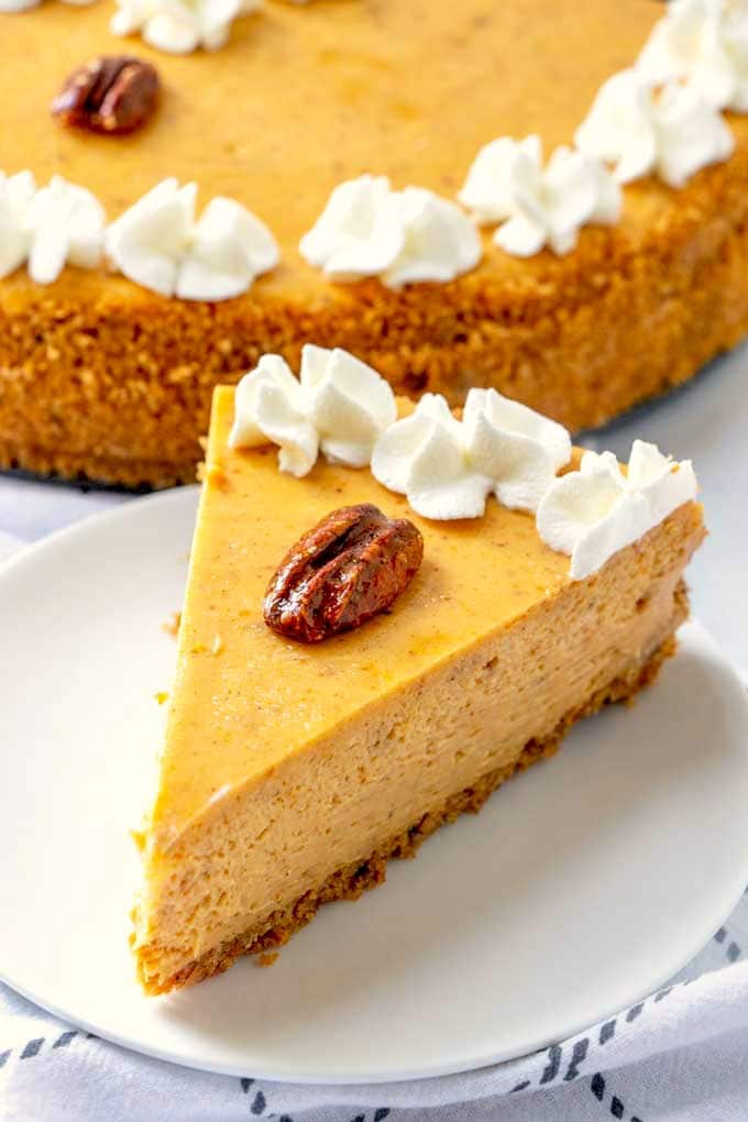 A slice of pumpkin cheesecake topped with a pecan and whipped topping. 