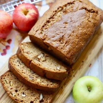 Sliced apple bread with pecans on a wooden butting board.