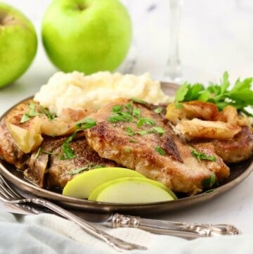 Pork chops and sliced apples on a plate with mashed potatoes.