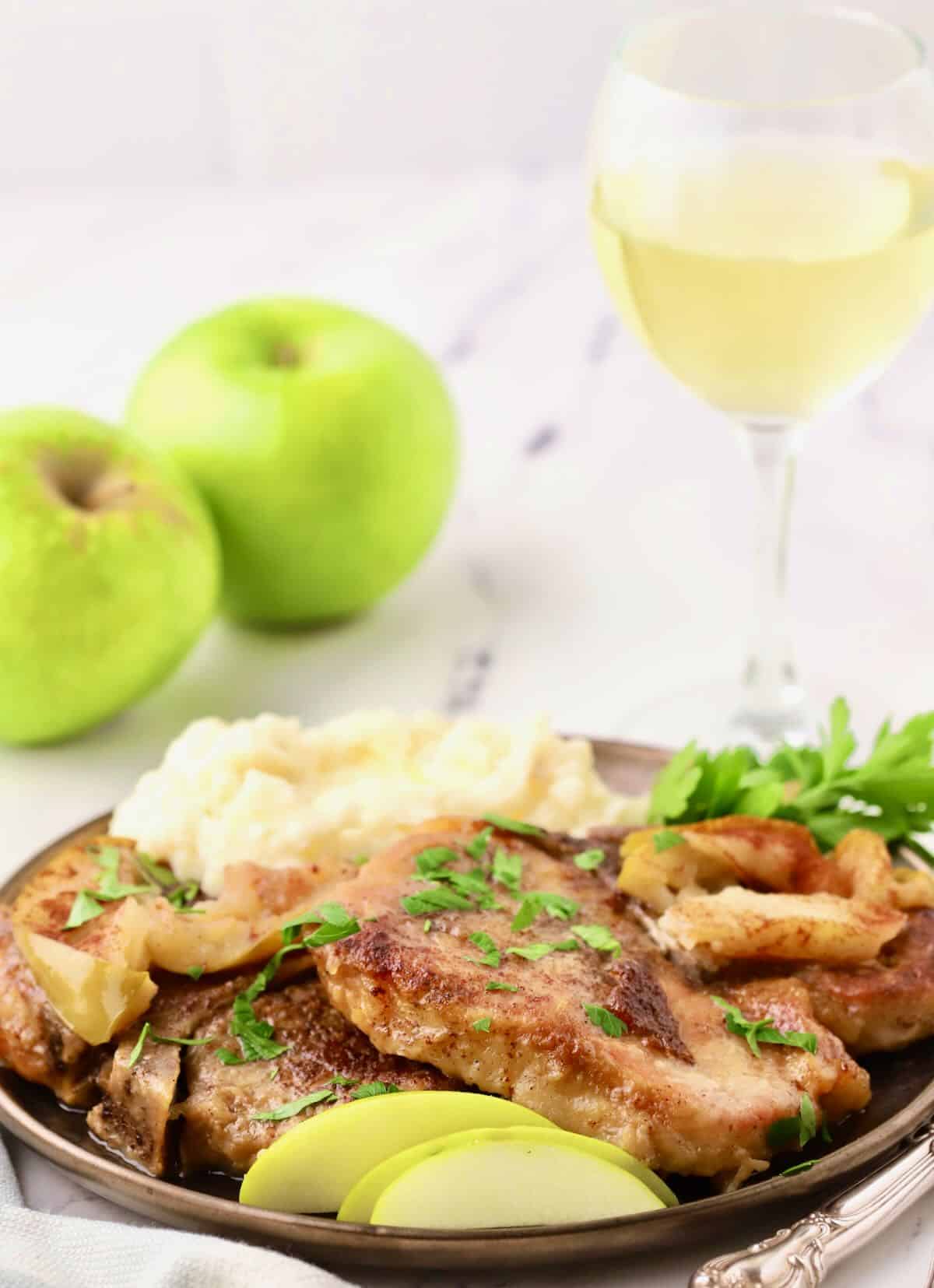 Two pork chops on a plate with a glass of white wine. 