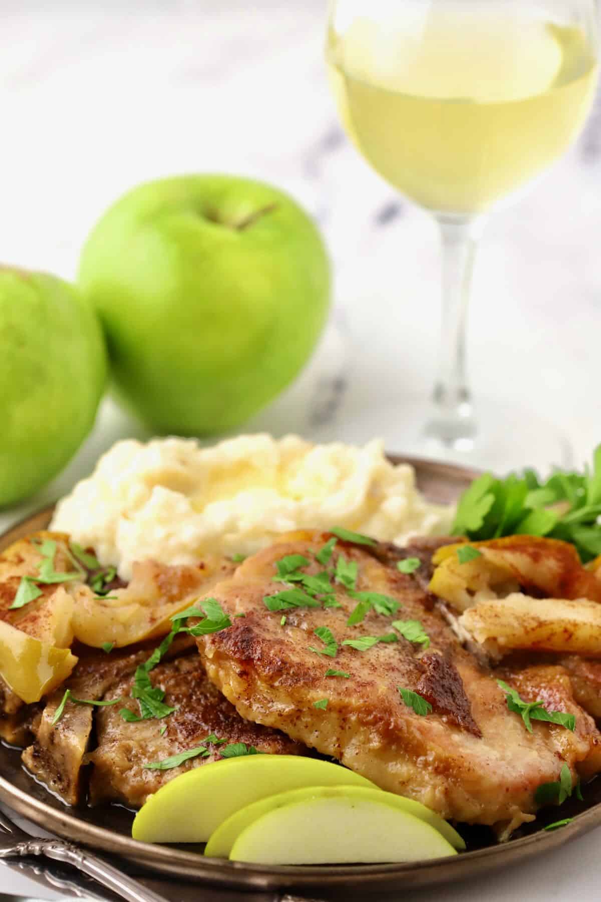 Pork chops on a plate with mashed potatoes and sliced apples. 