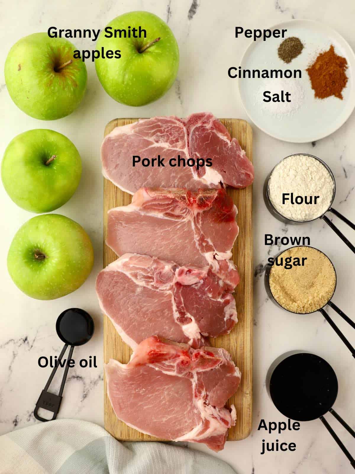 Raw pork chops on a cutting board along with apples and other ingredients. 