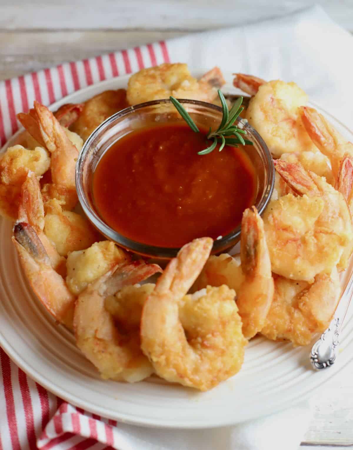 A plate with fried shrimp and a bowl of cocktail sauce. 