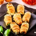 Mummy Jalapeño Poppers with googly eyes on a black plate.