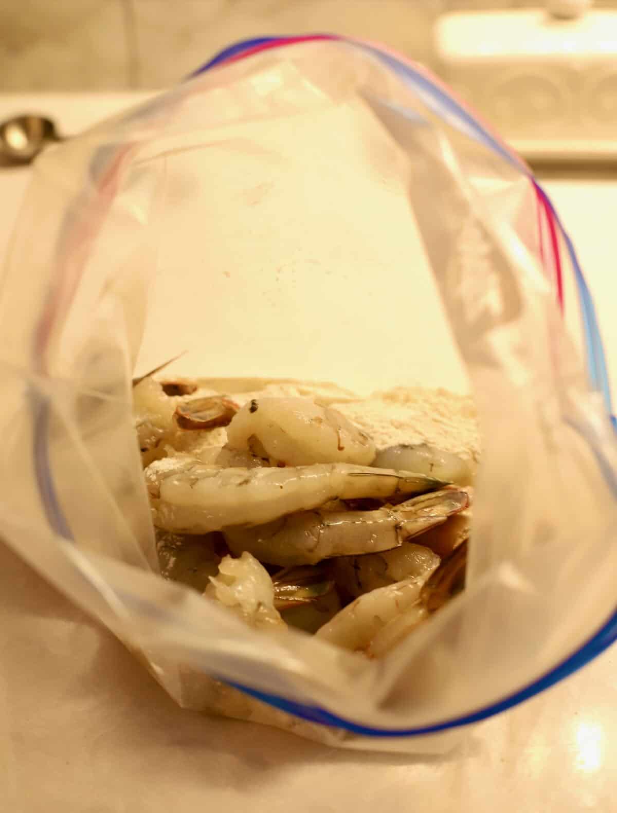 A plastic bag with seasoned flour and raw shrimp. 