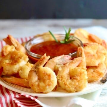 Fried shrimp and a bowl of cocktail sauce on a white plate.