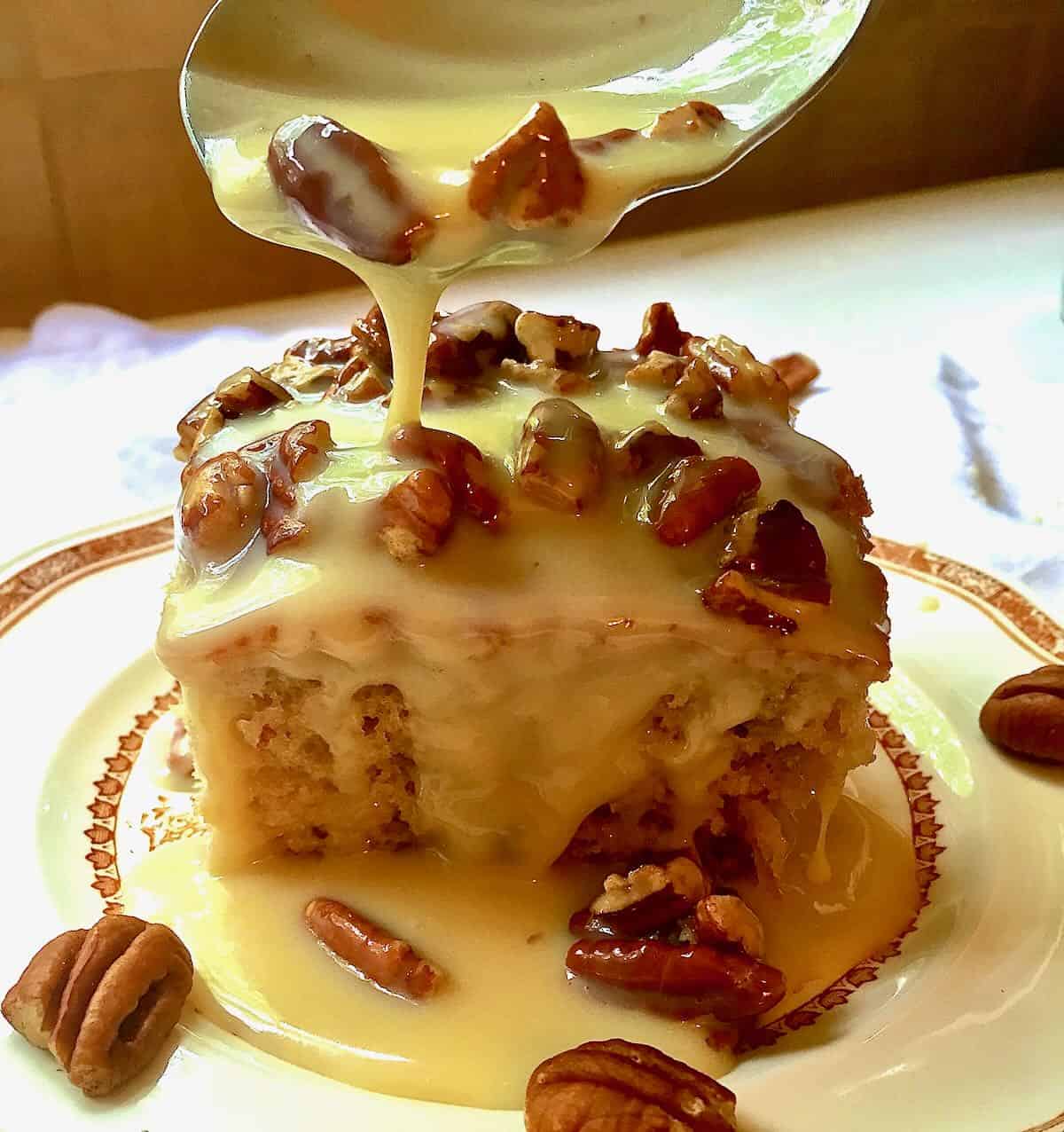 A square slice of pecan cake topped with pecans and glaze. 