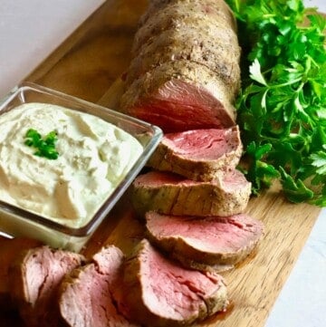A sliced beef tenderloin on a cutting board with gorgonzola dipping sauce.