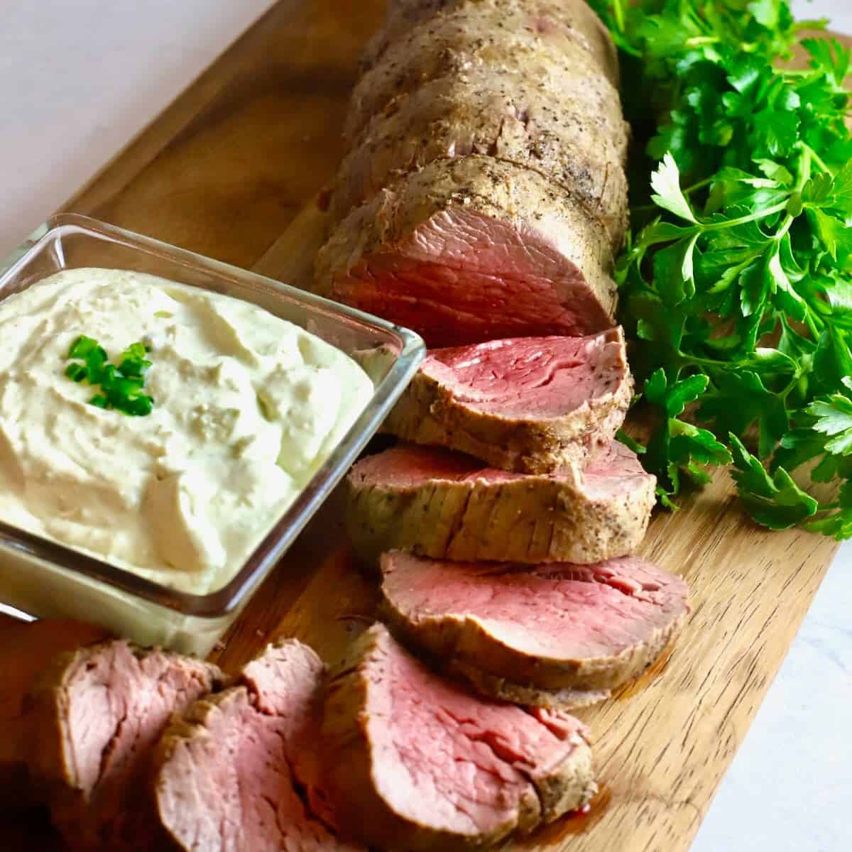 A sliced beef tenderloin on a cutting board with gorgonzola dipping sauce.