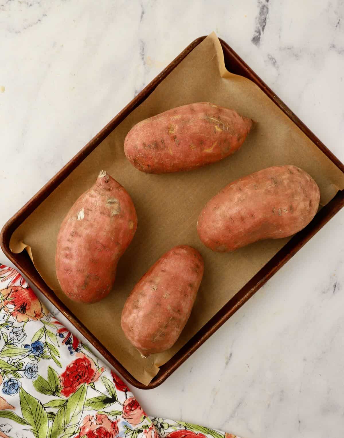 Four sweet potatoes on a baking sheet. 