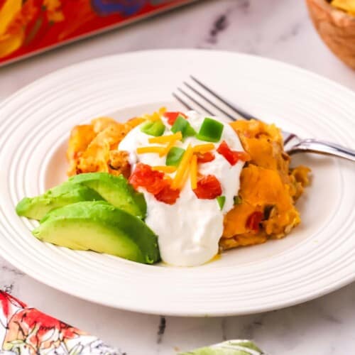 A serving of King Ranch Chicken Casserole on a plate topped with sour cream and diced tomatoes and bell pepper.
