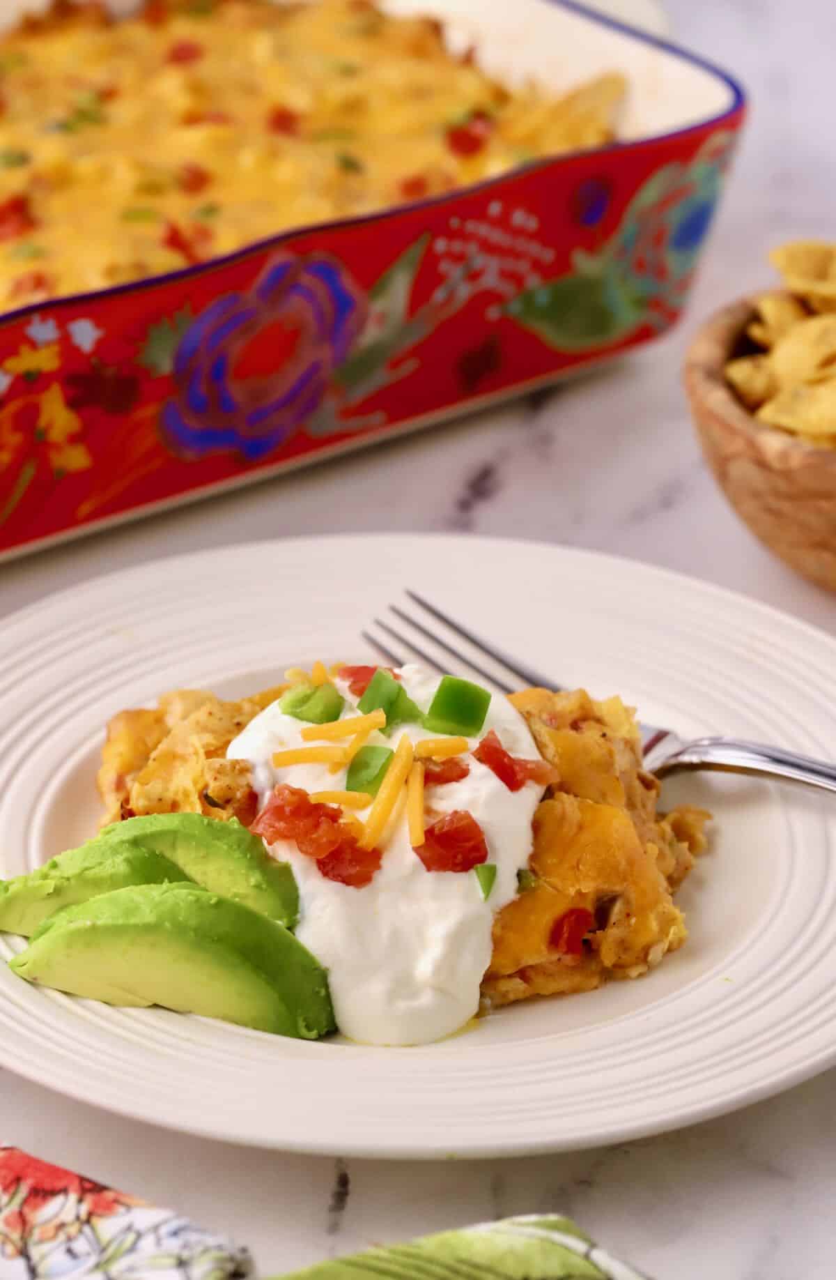 A serving of chicken casserole topped with sour cream, shredded cheese, tomatoes and bell pepper. 