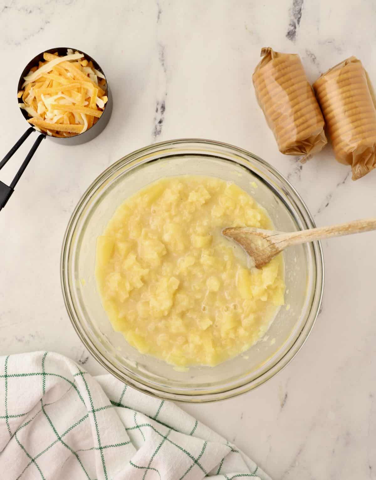 Pineapple mixture in a glass bowl with shredded cheese and crackers above it. 