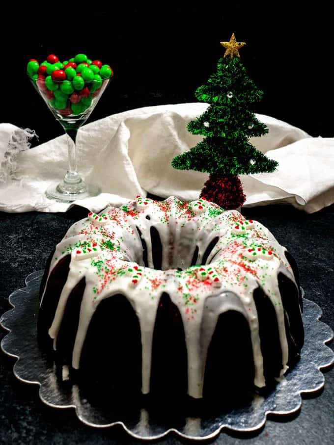 A Christmas Bundt Cake on a platter covered with glaze and red and green sprinkles.