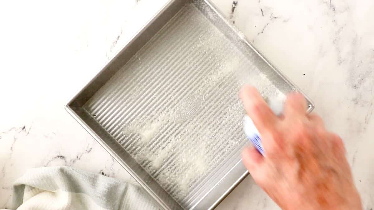 Spraying a square baking pan with non-stick-baking spray.