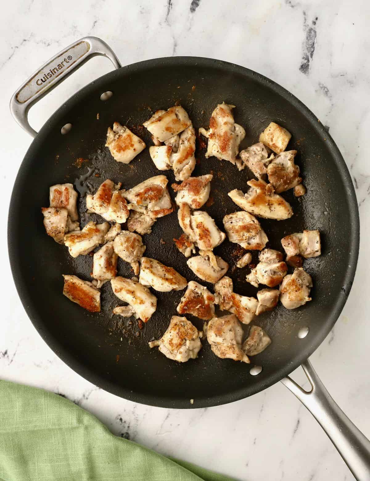 Cut up pieces of chicken cooking in a skillet. 