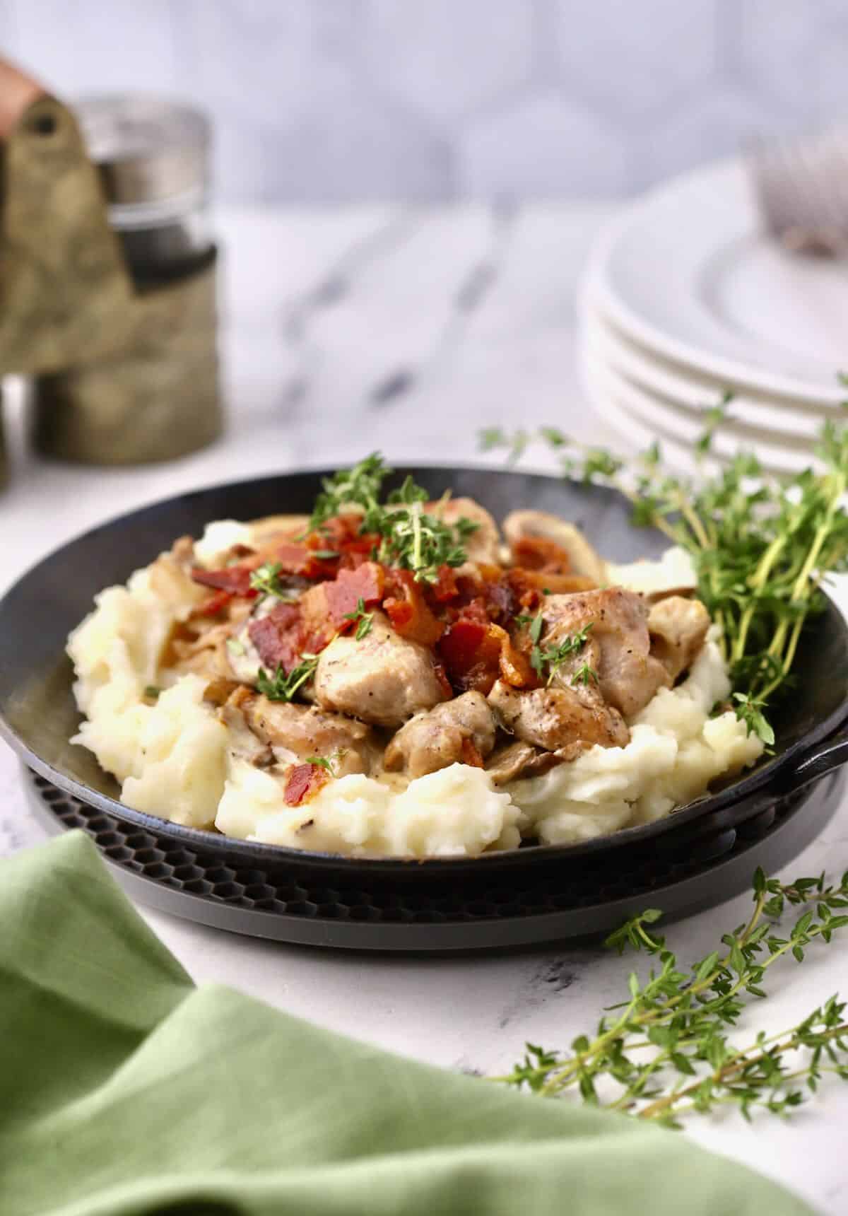 A small skillet full of mashed potatoes, chicken, bacon and mushrooms. 
