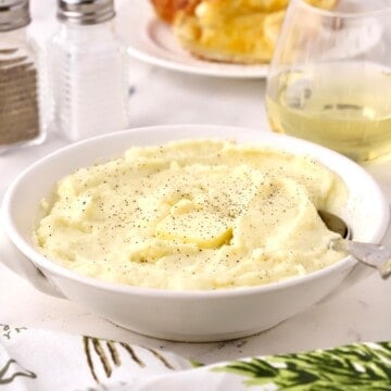 A white serving dish full of mashed potatoes topped with a pat of butter.