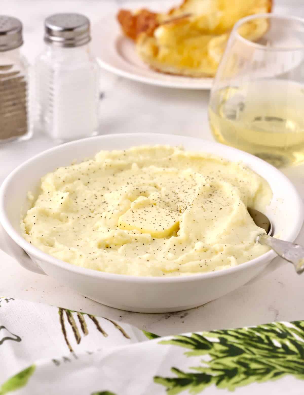 A white serving bowl full of mashed potatoes topped with a pat of butter. 