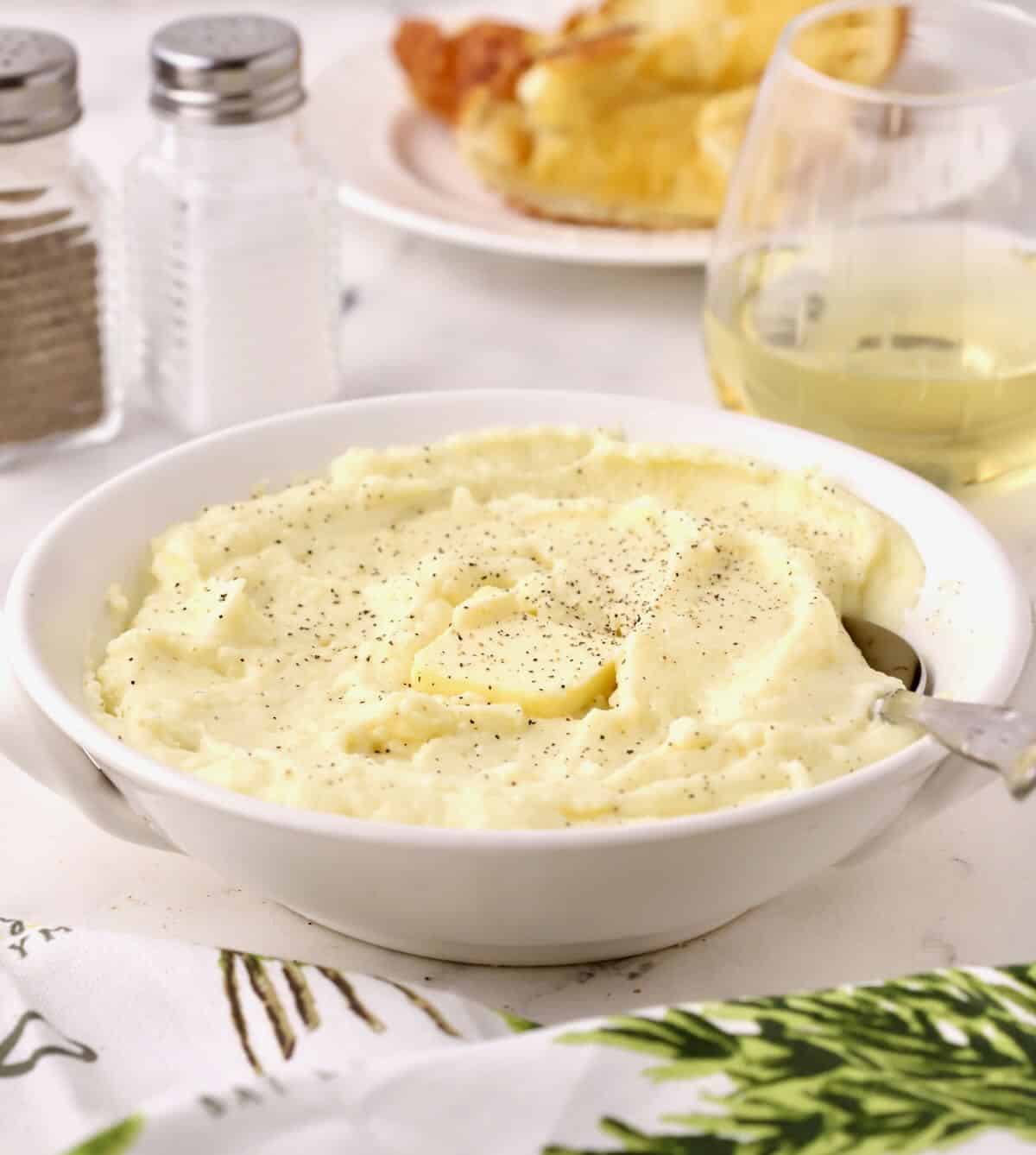 A bowl of mashed potatoes topped with a pat of butter with a spoon. 