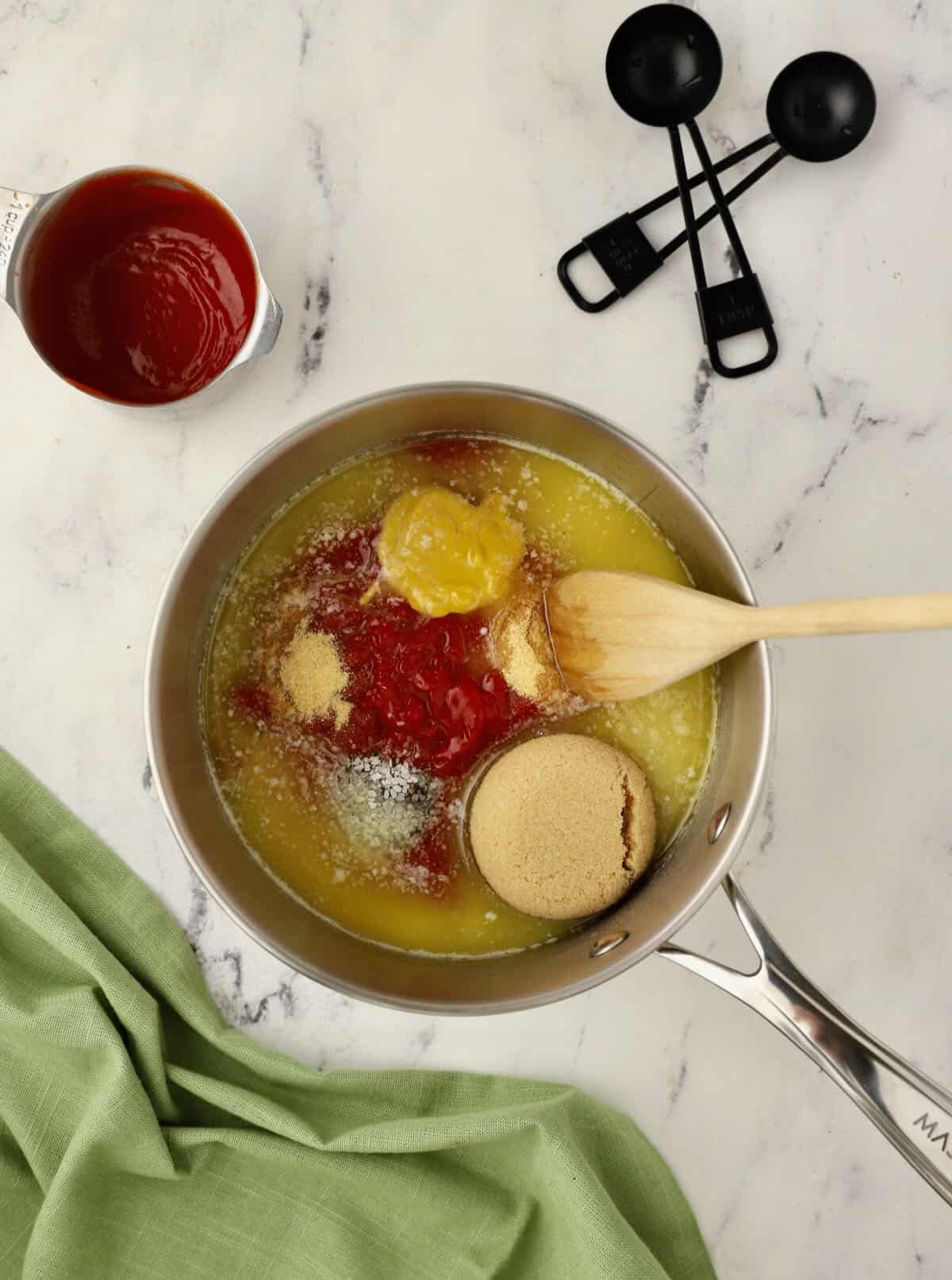 A saucepan with ketchup, brown sugar, mustard and butter in it. 