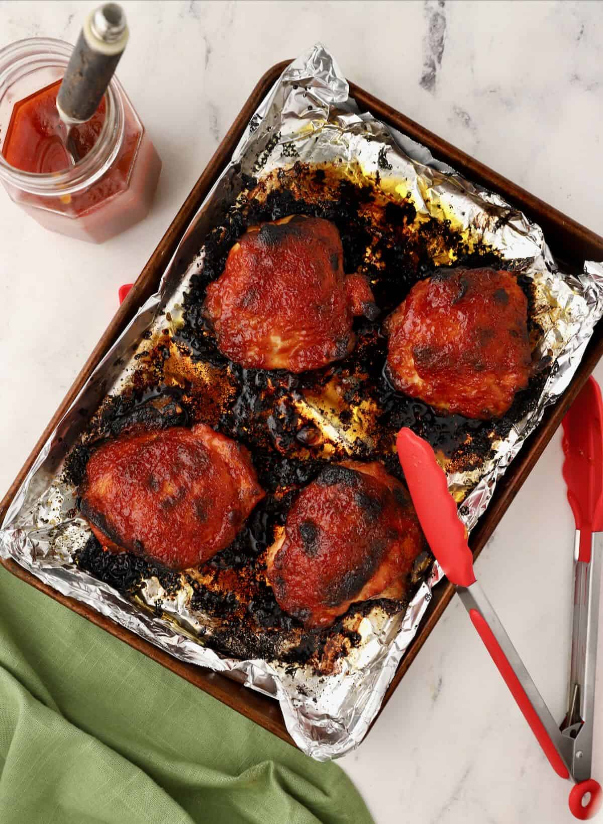 Four chicken thighs covered with barbecue sauce baked in the oven. 