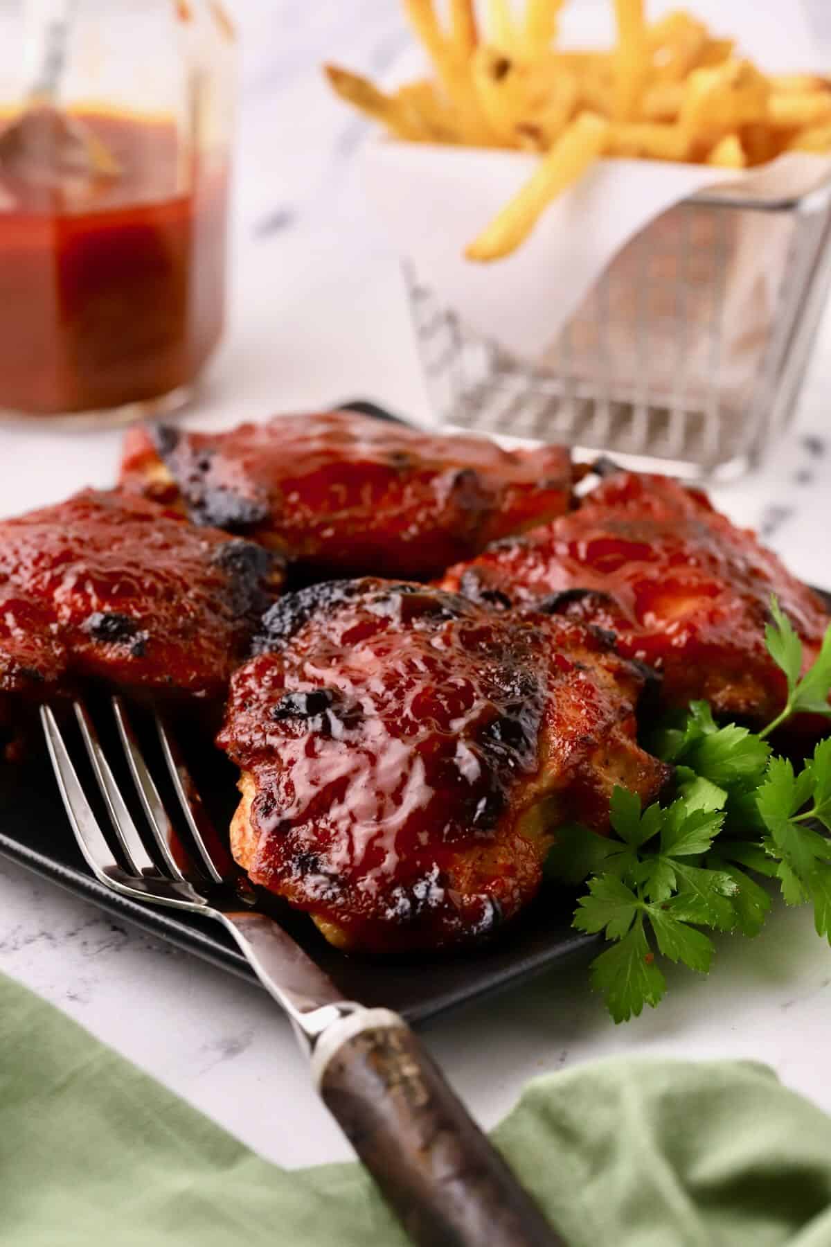 Four oven baked barbecued chicken thighs on a black plate with a fork. chicken thigh