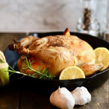 A roasted chicken in a cast iron skillet garnished with lemon slices.