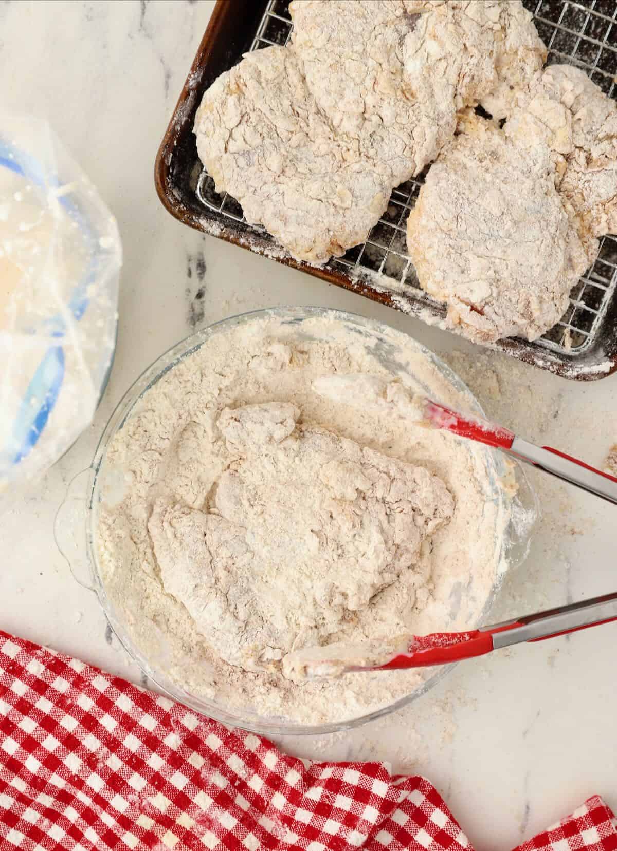 Chicken thighs being dredged in flour and then placed on a wire rack. 