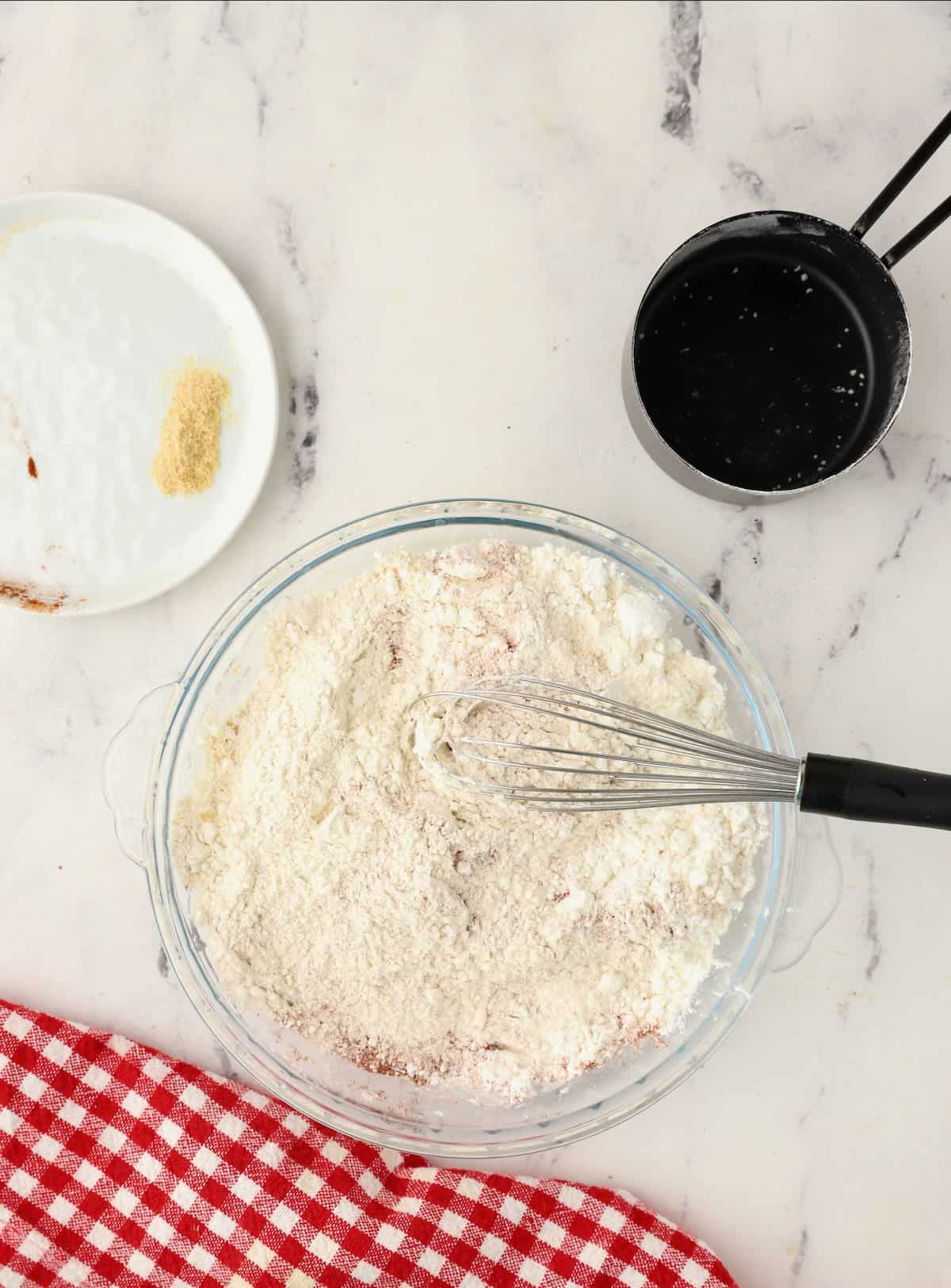 A pie plate with flour and seasoning being whisked together. 