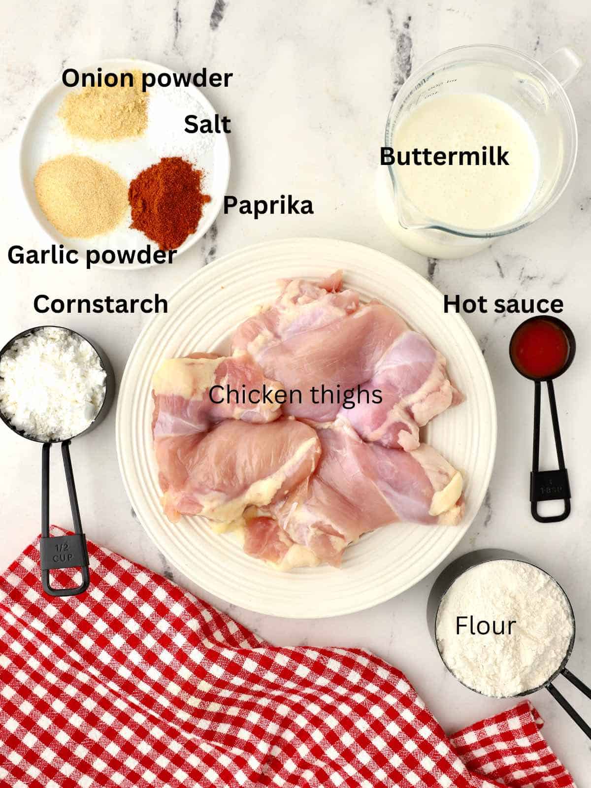 Ingredients for fried chicken thighs including thighs, flour, cornstarch, buttermilk and seasonings.