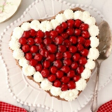 A heart-shapped chocolate cake topped with cherries.