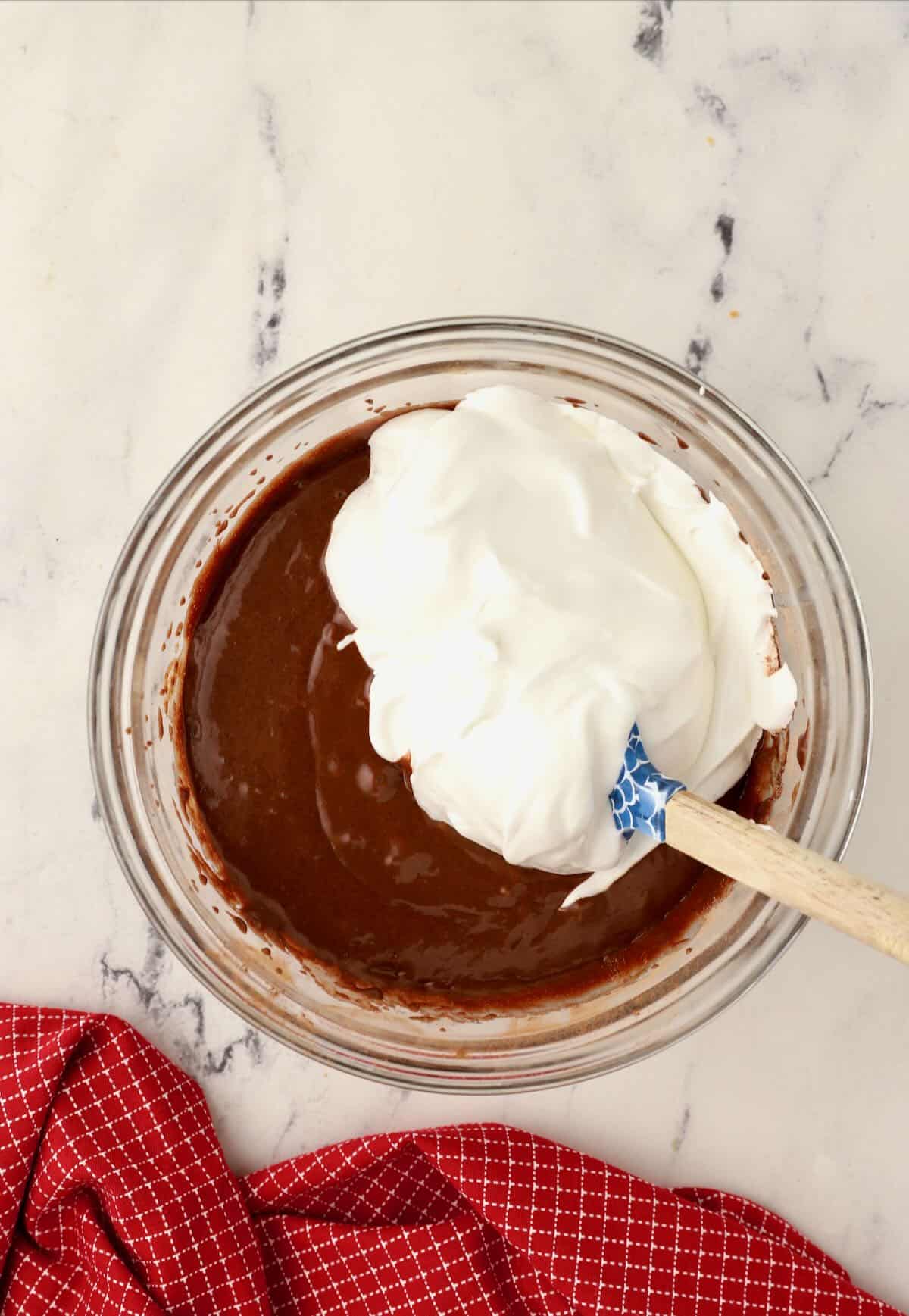 Adding meringue to chocolate cake batter in a bowl. 