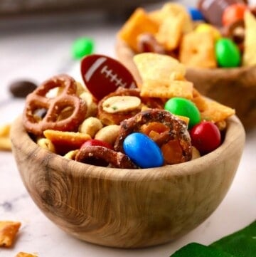 A wooden bowl with a snack mix made with pretzels, Bugles, Cheez-its, and M&Ms.