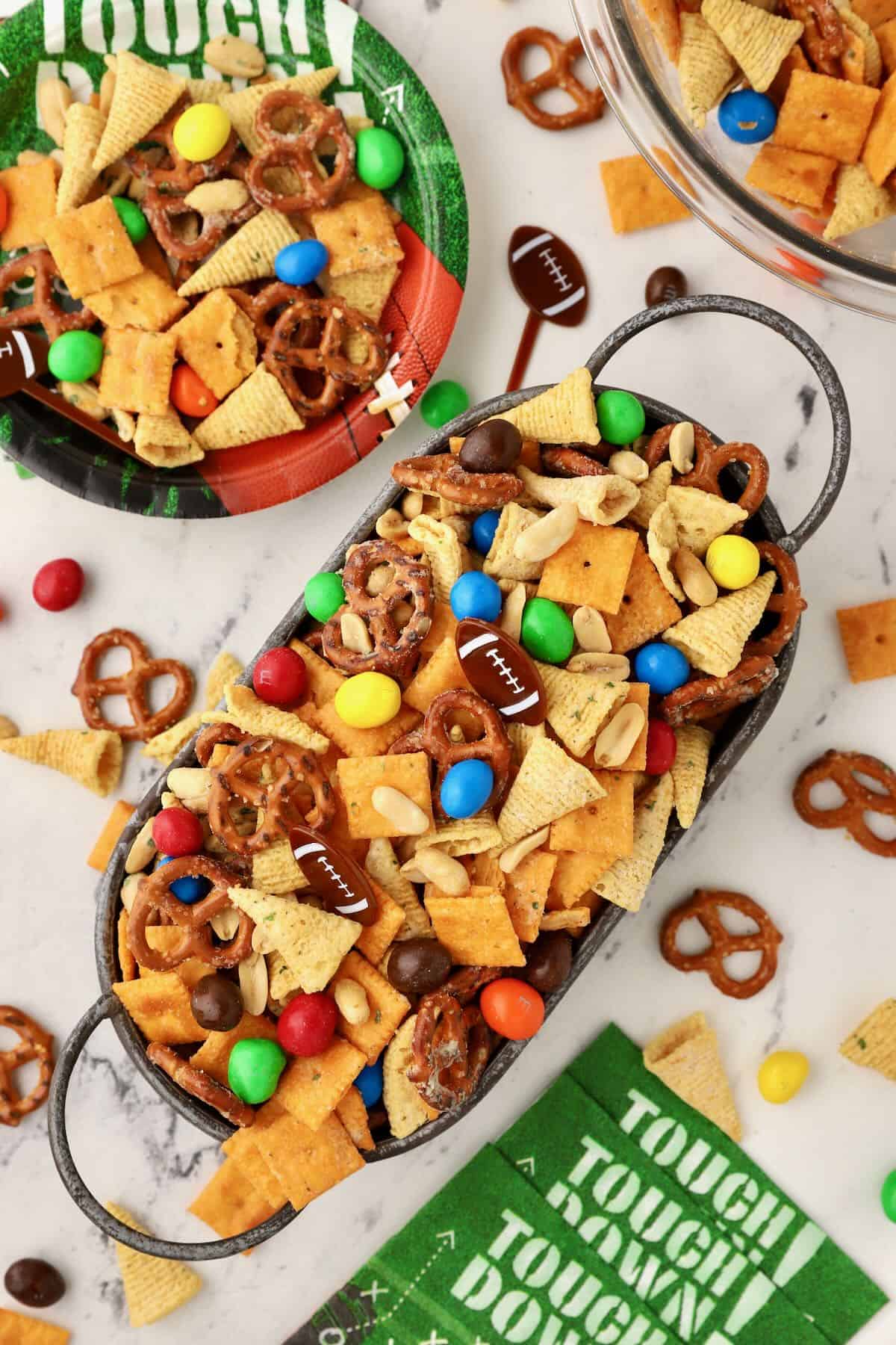 An oval metal bowl full of snack mix with Cheeze-its, and Bugles. 