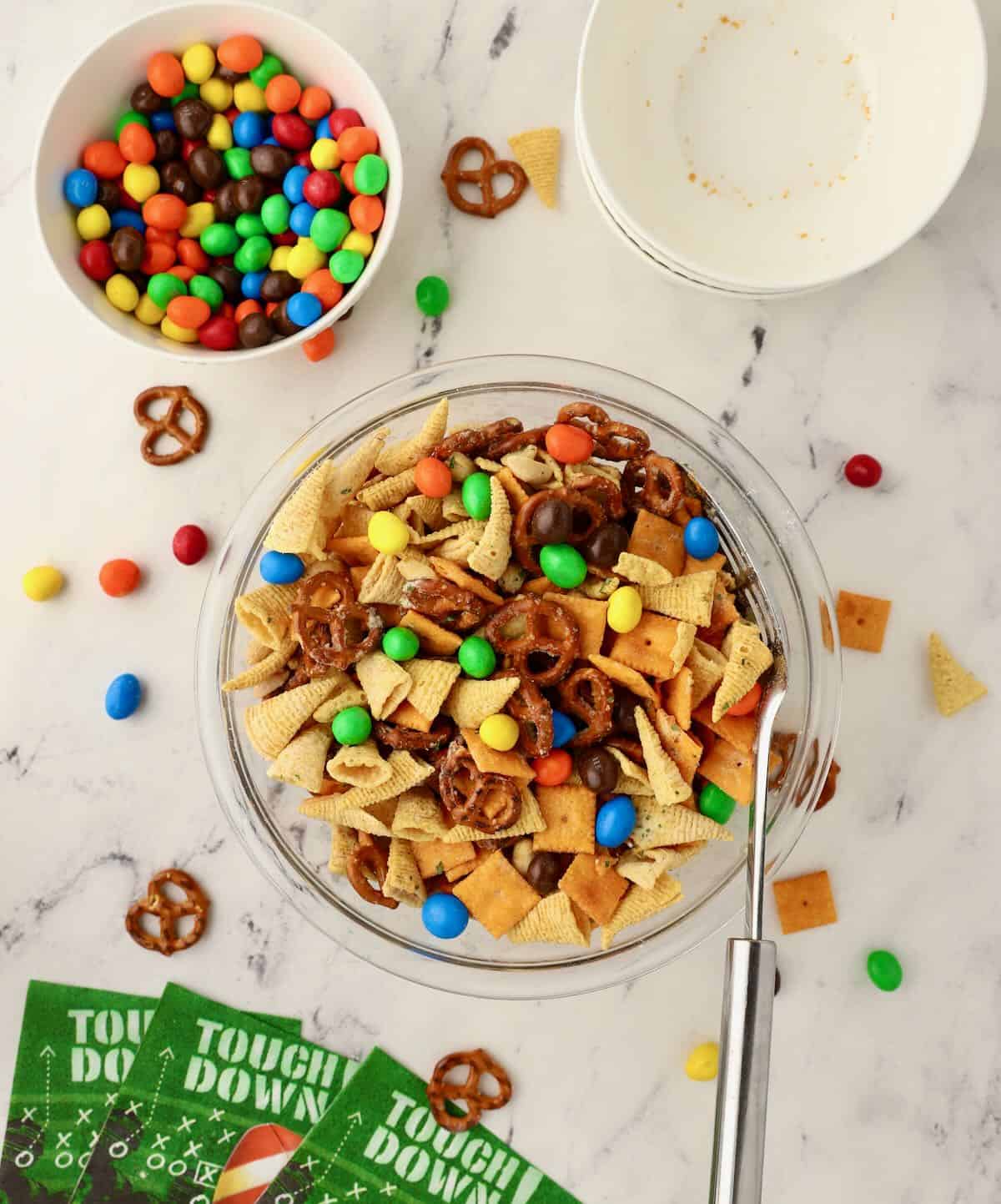 A large glass bowl with game day snack mix topped with M&Ms. 