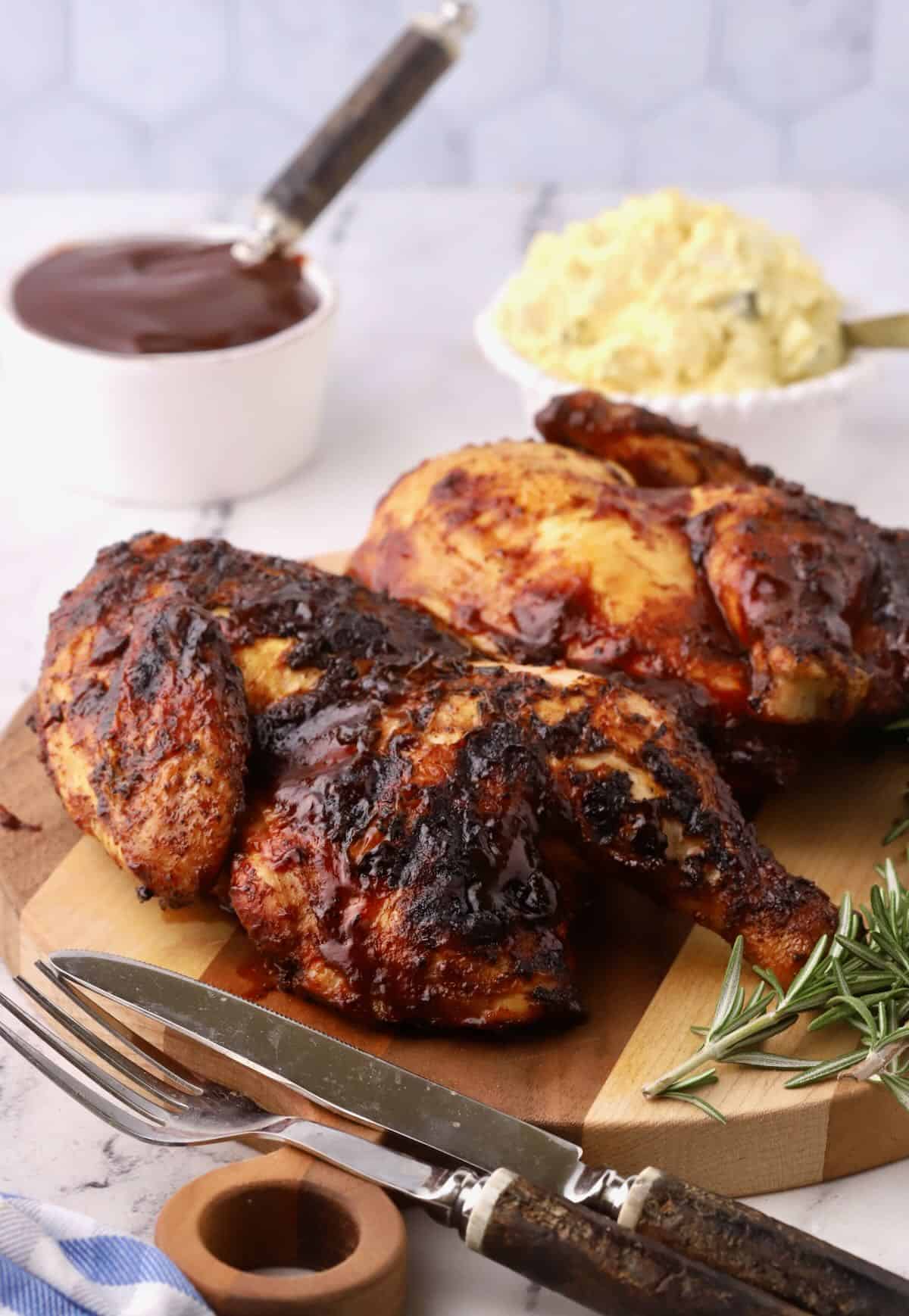 Two grilled chicken halves with barbecue sauce on a wooden cutting board. 