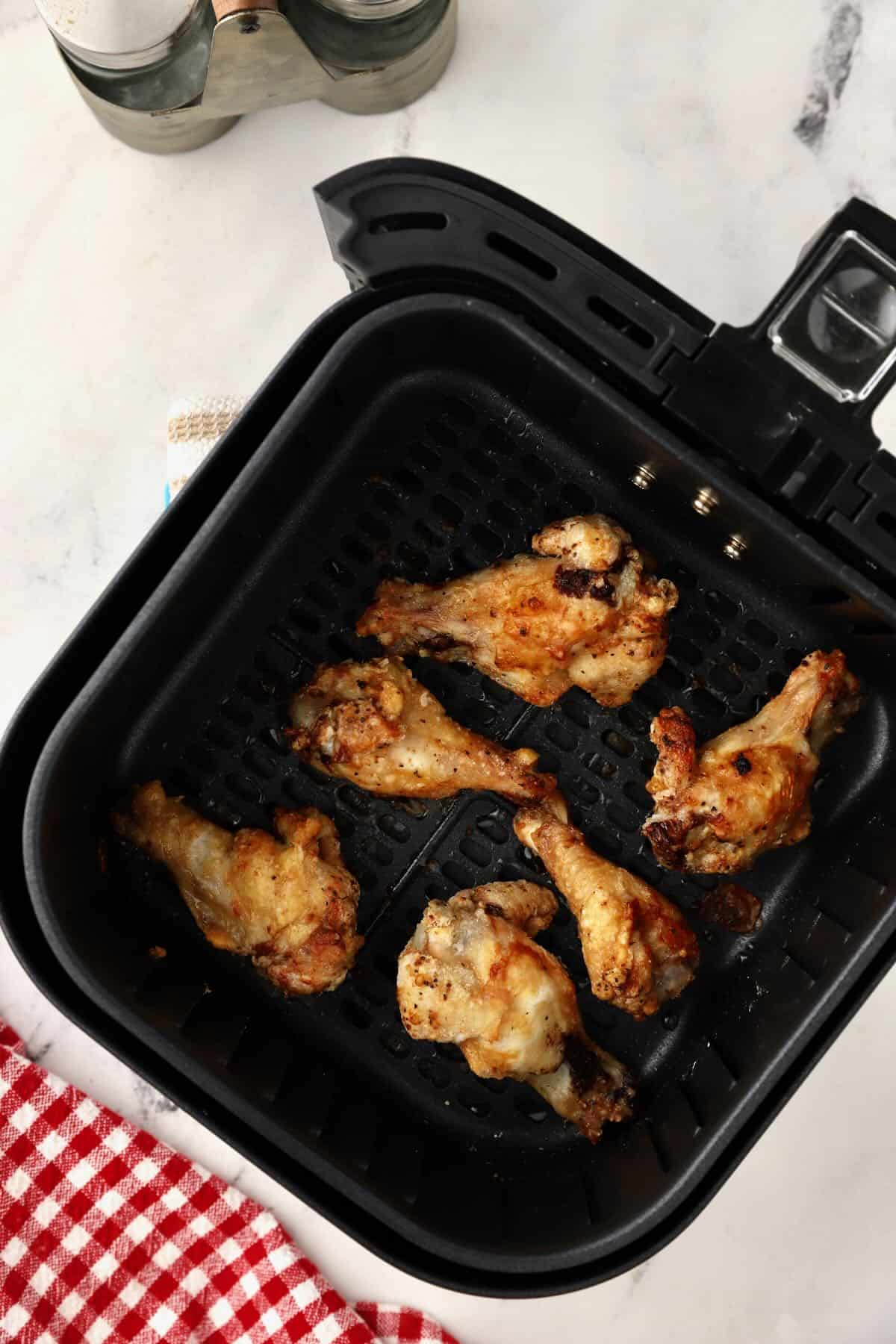 Partially cooked chicken wings in an air fryer basket. 