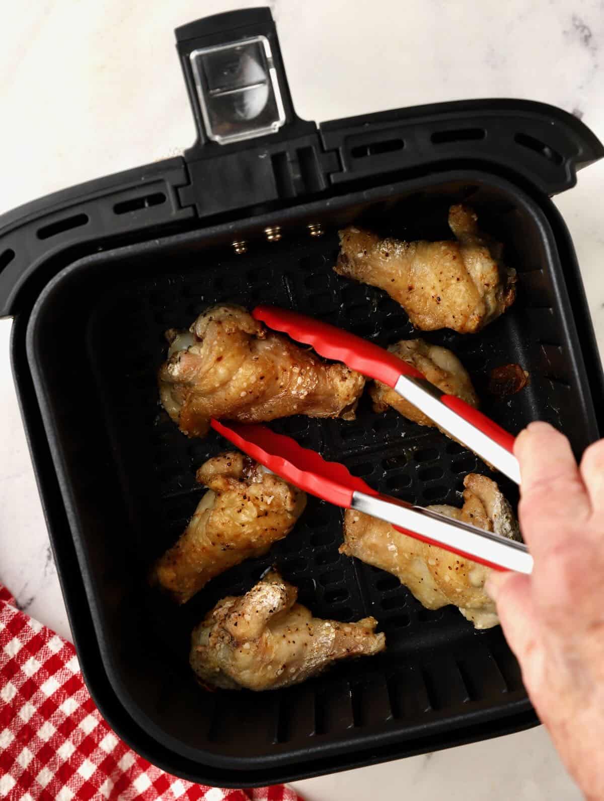 Turning chicken wings over in the basket of an air fryer. 